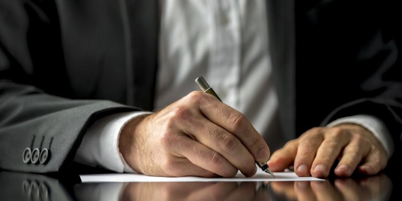 Close-up of hands in suit jacket writing on paper with pen—formal setting for contracts or paperwork