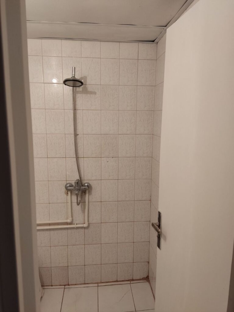 An old shower area with outdated tiles and exposed plastic plumbing pipes before a complete modern renovation by Fardo Technical Services.