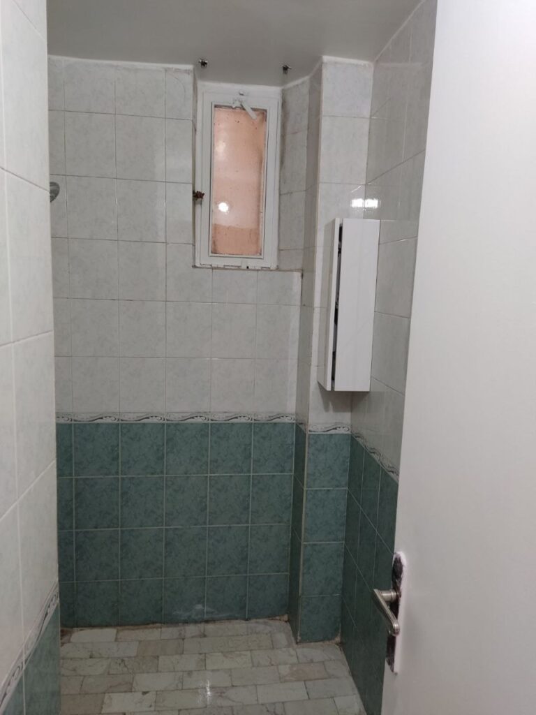 An outdated bathroom with old green and white tiles and traditional flooring before a complete modern renovation by Fardo Technical Services.